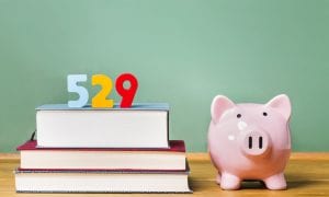529 numbers on top of stack of books with piggy-bank next to it in front of chalkboard