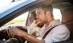 Man eating sandwich in car while driving with one hand