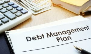 Debt Management Plan written on notepad lying on table with money and calculator in background