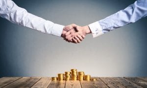 Two people shaking hands over pile of coins