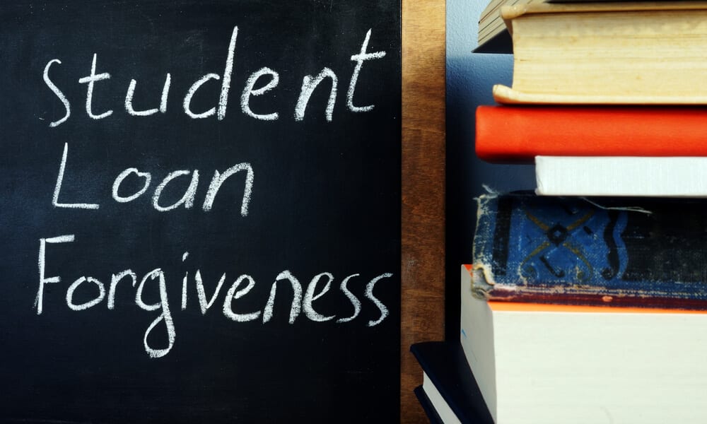Student loan forgiveness written on blackboard next to stack of books