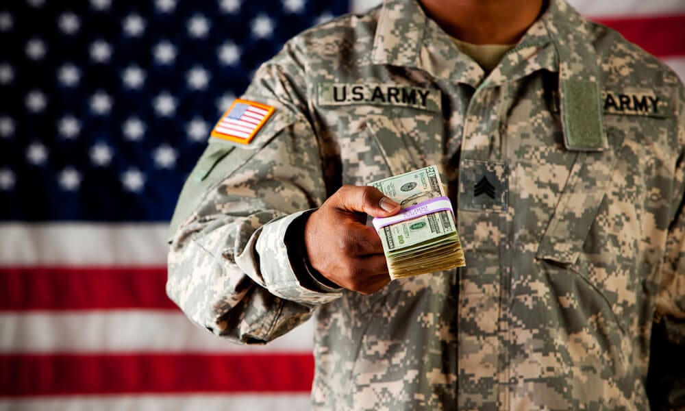 Soldier in uniform holding out stack of cash
