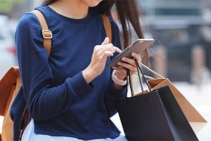 Woman carrying shopping bags using her phone to buy items now and pay later